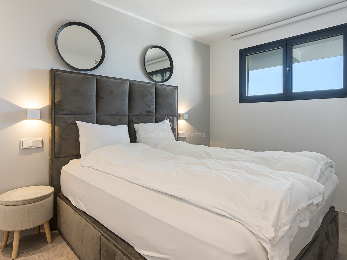 Chambre moderne avec tête de lit en velours gris, miroirs ronds, appliques murales et fenêtre à cadre noir.