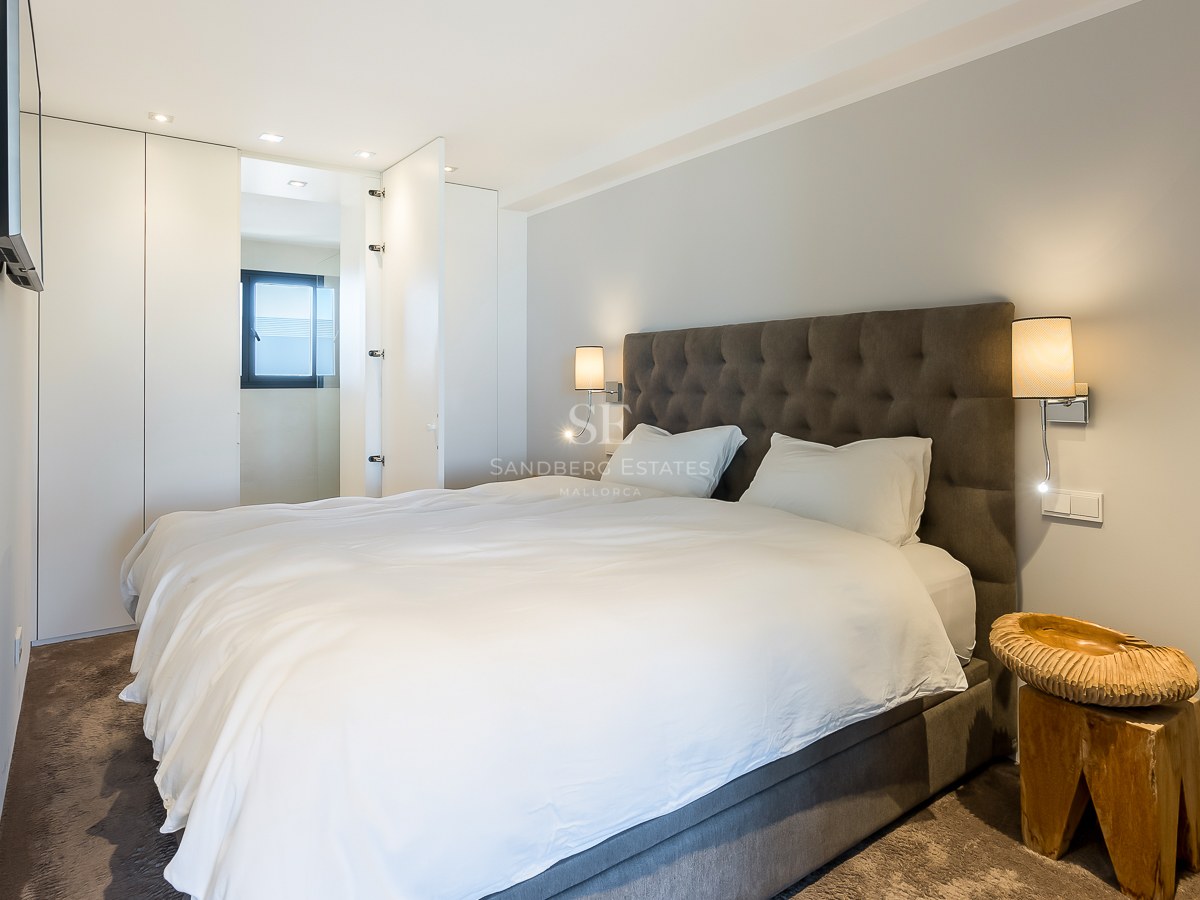 Chambre moderne avec tête de lit capitonnée grise, placards intégrés blancs et table de chevet en bois sculpté.