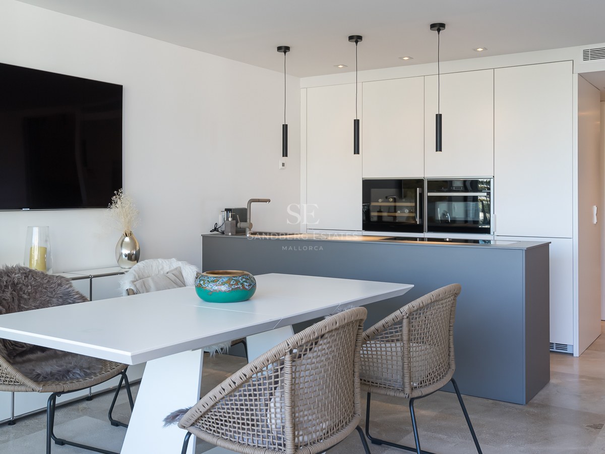 Cuisine moderne avec îlot gris, armoires blanches sans poignées et espace repas avec sol en pierre naturelle.