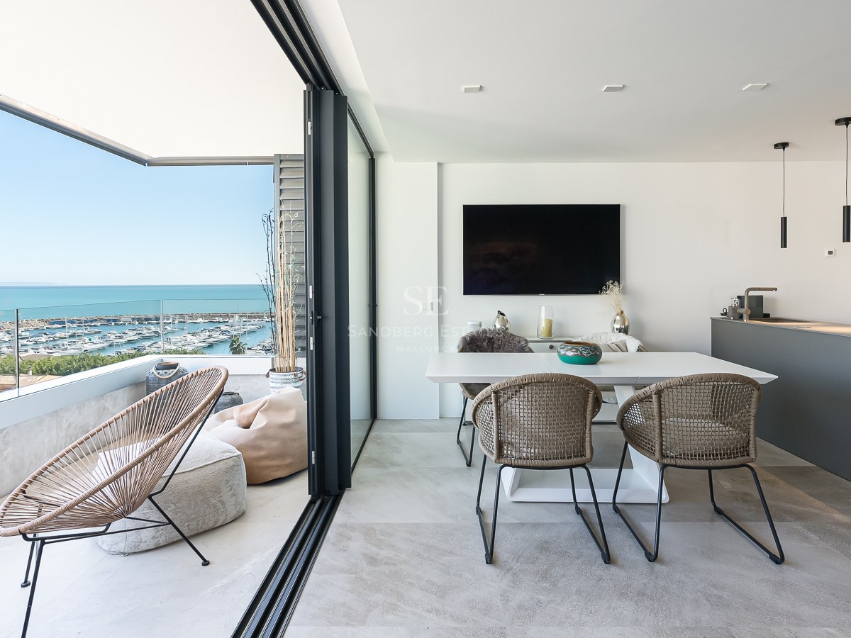 Salle à manger moderne et terrasse avec garde-corps en verre surplombant un port de plaisance et la mer Méditerranée.