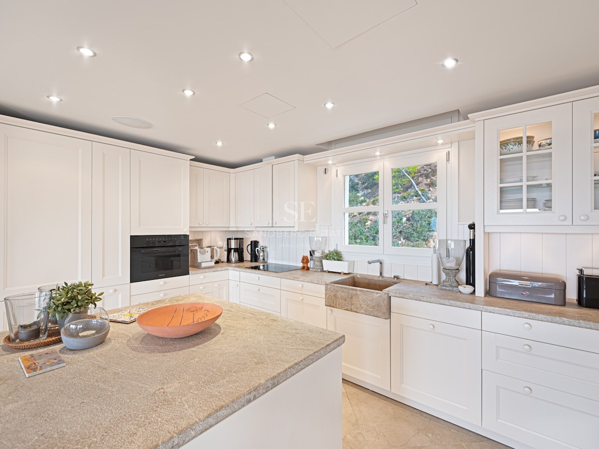 Bright kitchen featuring white shaker cabinets, natural stone countertops, and integrated premium appliances.