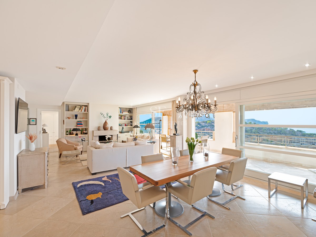 Bright open-plan living and dining room with marble floors, wooden table, and large windows overlooking the Mediterranean.