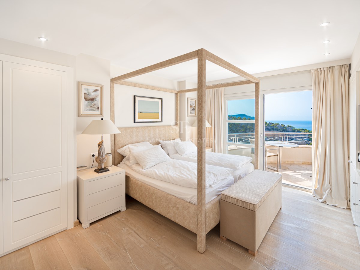 Master bedroom featuring a light wood canopy bed, white bedding, and sliding glass doors opening to a sea-view terrace.