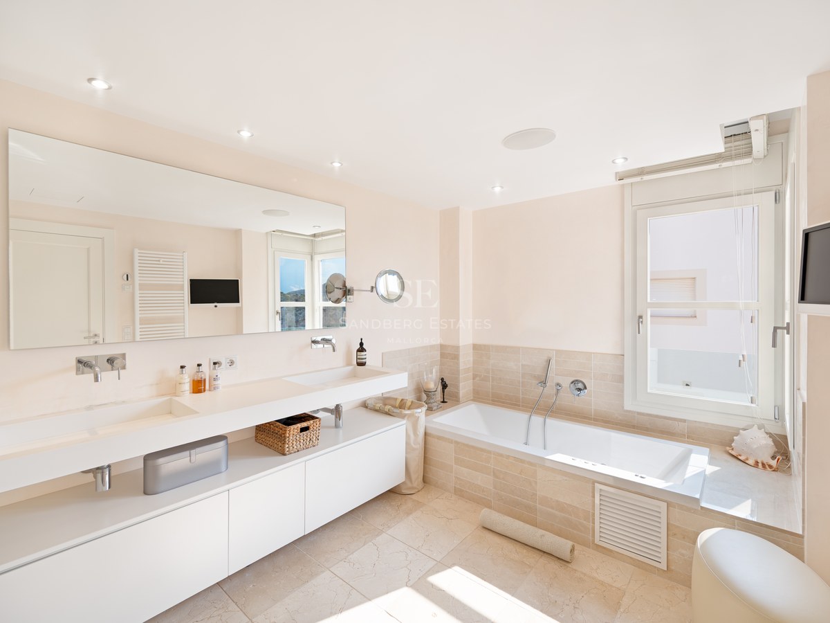 Bright master bathroom featuring a floating double vanity, large wall mirror, and built-in tub with neutral stone tiling.