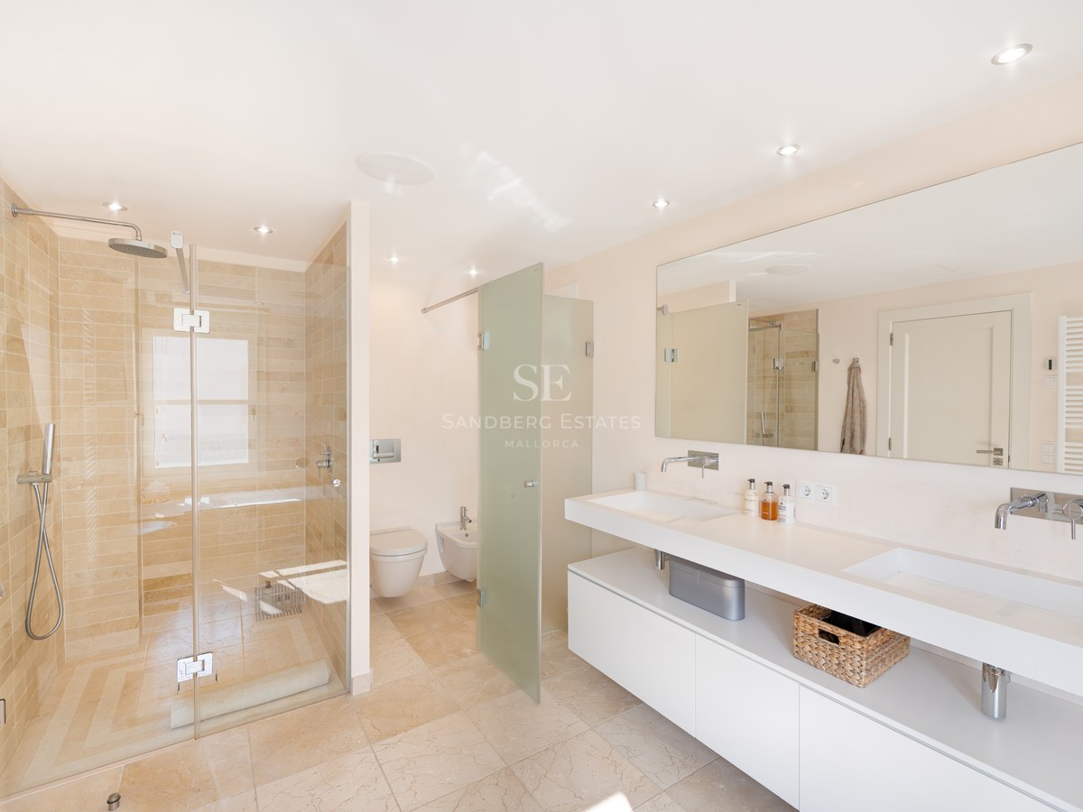 Bright bathroom featuring a double white vanity, large mirror, and walk-in shower with beige natural stone tiling.