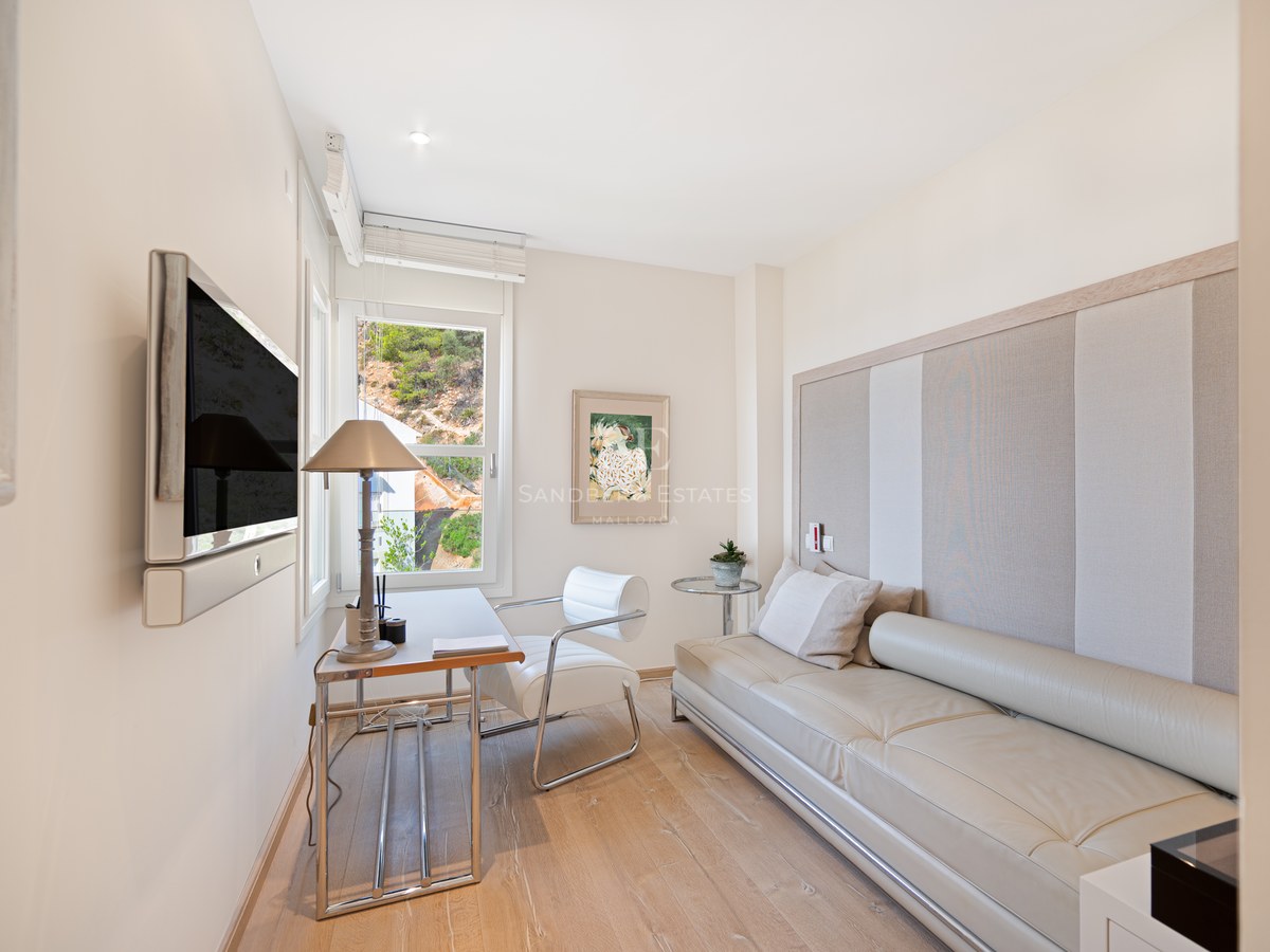 Bright home office featuring light wood floors, white leather sofa, glass desk, and a window showing greenery.