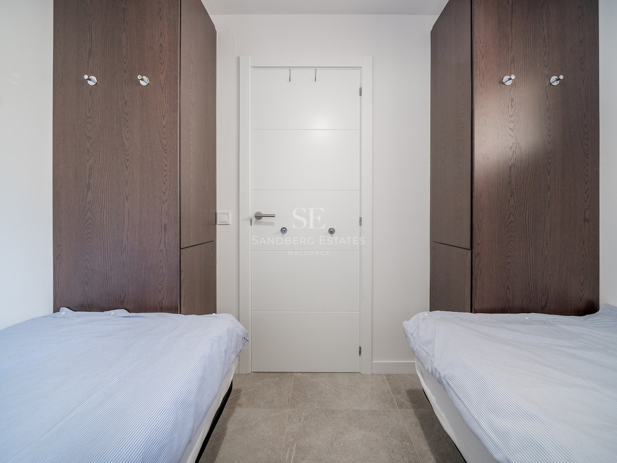Chambre contemporaine avec lits jumeaux, placards en bois sombre et sol en carrelage gris.
