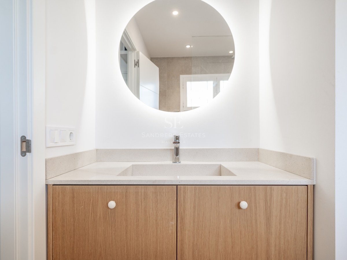 Vanité de salle de bain moderne avec miroir LED circulaire, ébénisterie en bois clair et lavabo blanc.
