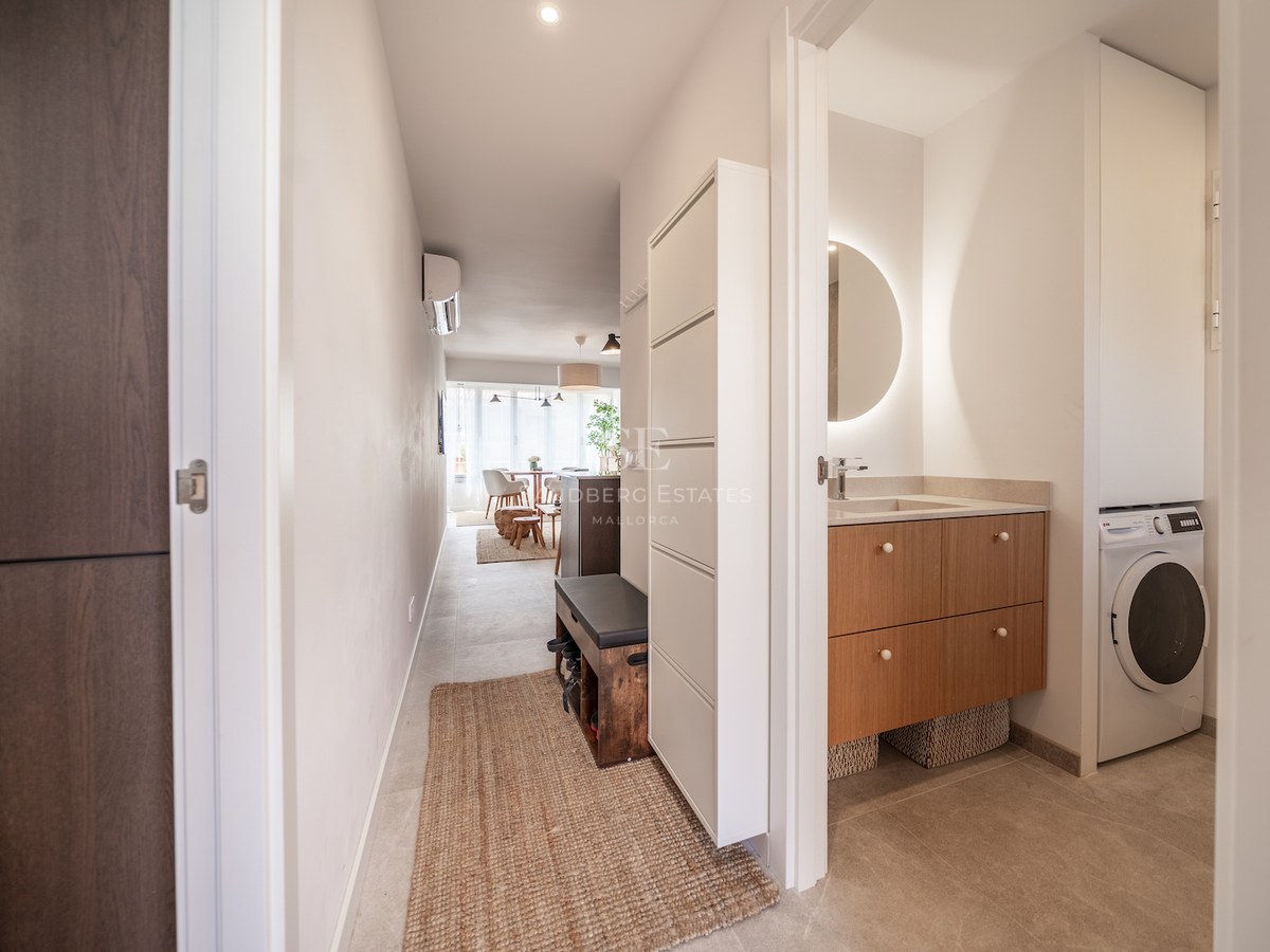 Couloir moderne avec meubles en bois clair, miroir rétroéclairé et tapis en fibres naturelles.