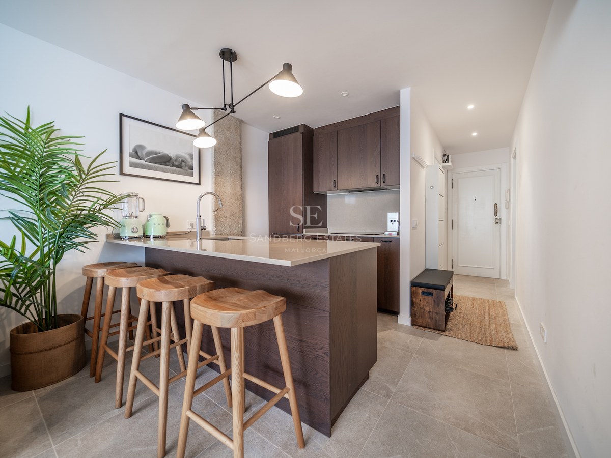 Cuisine moderne avec placards en bois sombre, îlot en pierre avec quatre tabourets et suspension industrielle.