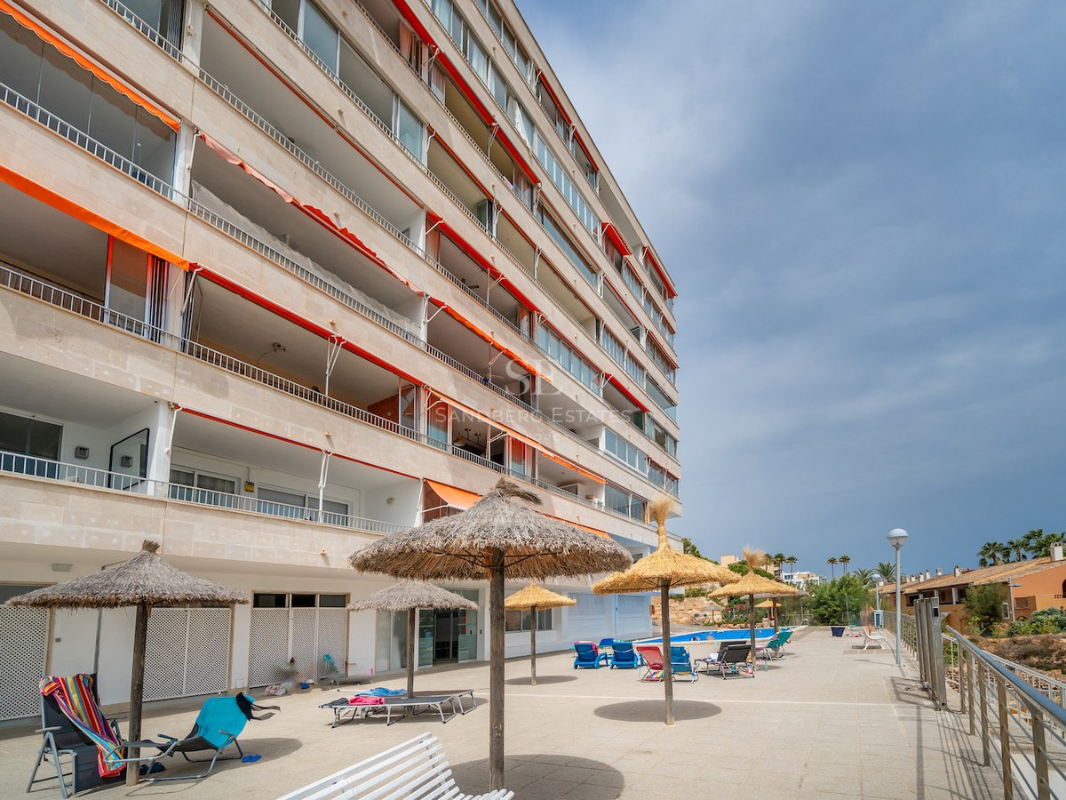 Immeuble d'appartements avec balcons, stores orange et espace piscine avec parasols en paille.