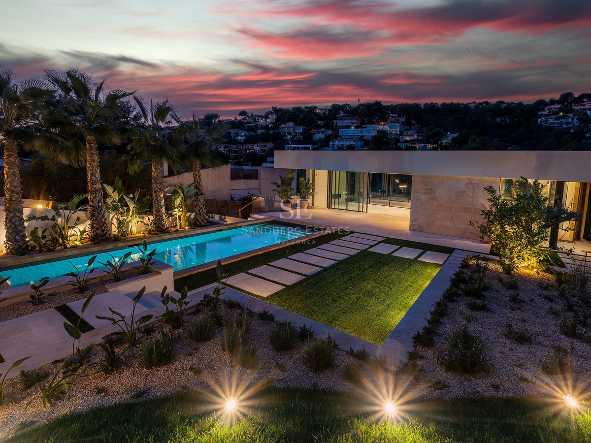 Dusk view of a contemporary villa with an illuminated swimming pool, palm trees, and a dramatic sunset sky.