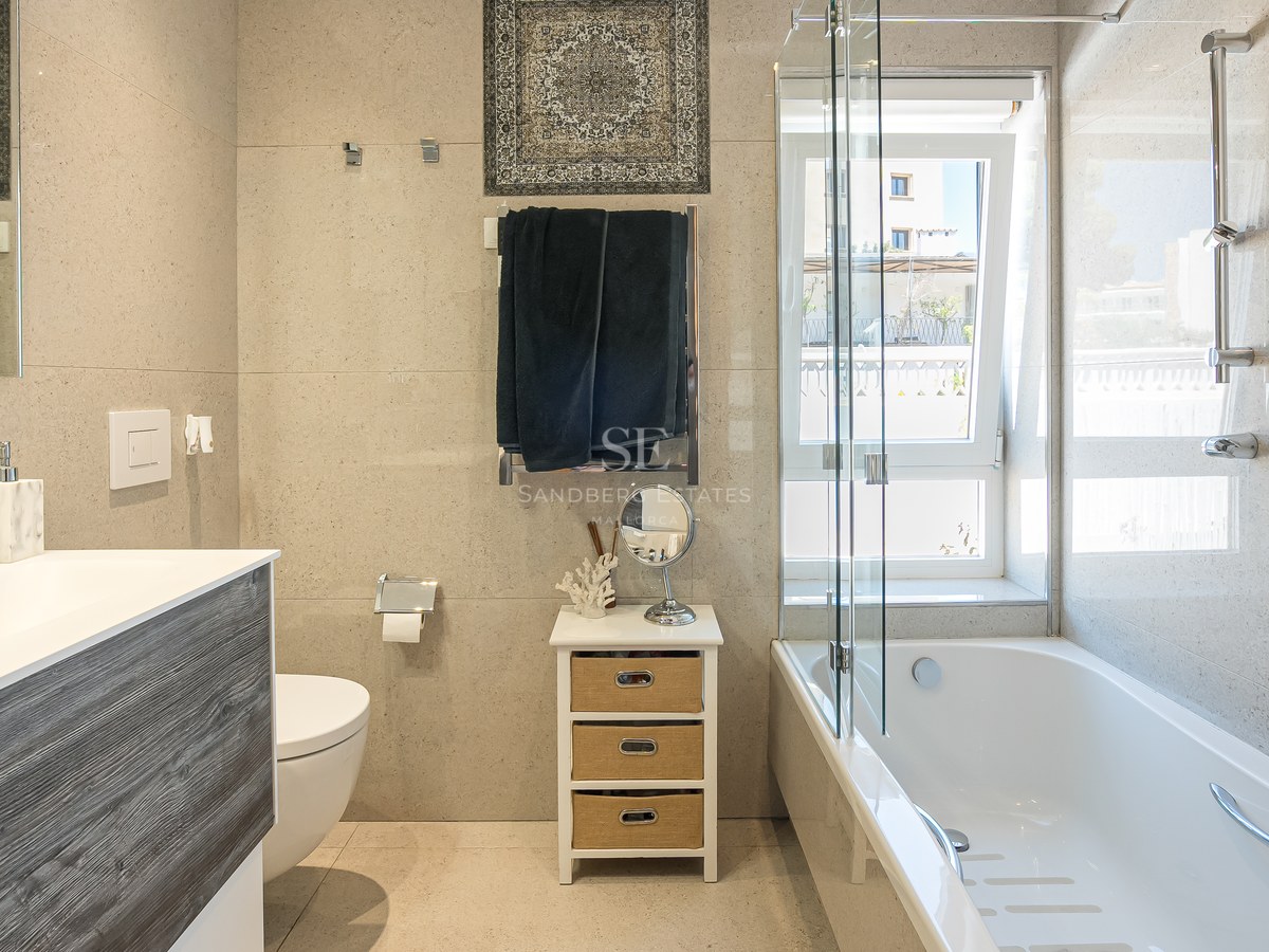 Salle de bain moderne avec baignoire blanche, paroi en verre, meuble en bois et carrelage mural effet pierre naturelle.