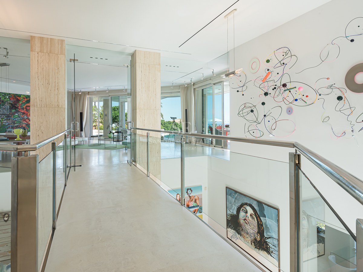 A modern upper-floor gallery featuring glass railings, travertine columns, and large-scale contemporary wall art.