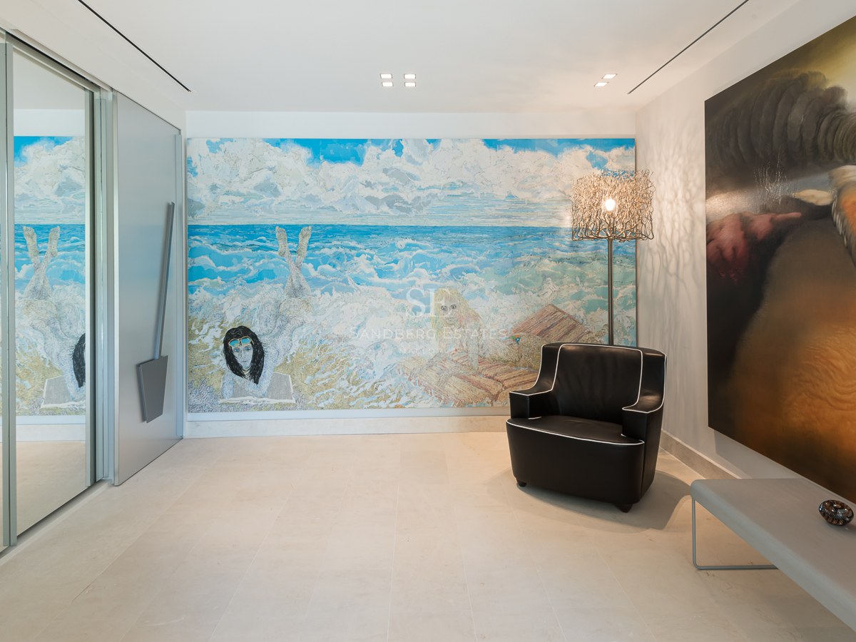 Modern hallway featuring large-scale paintings, a black leather armchair, and light natural stone flooring.