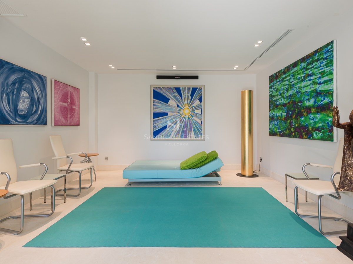 Modern relaxation room featuring a turquoise rug, an Oriental bronze statue, vibrant abstract art, and minimalist white seating.