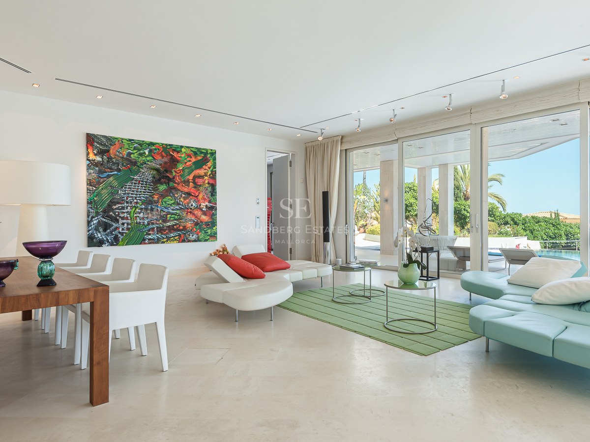 Bright living room with floor-to-ceiling glass doors opening to a terrace, pool, and sea view.