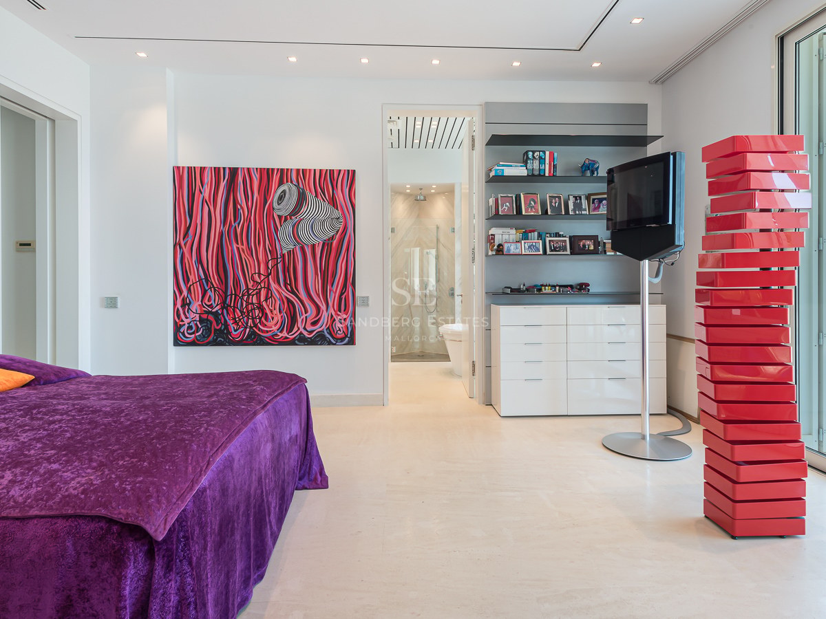 Modern bedroom with purple velvet bed, large abstract red painting, red sculpture, and glass doors to a terrace.