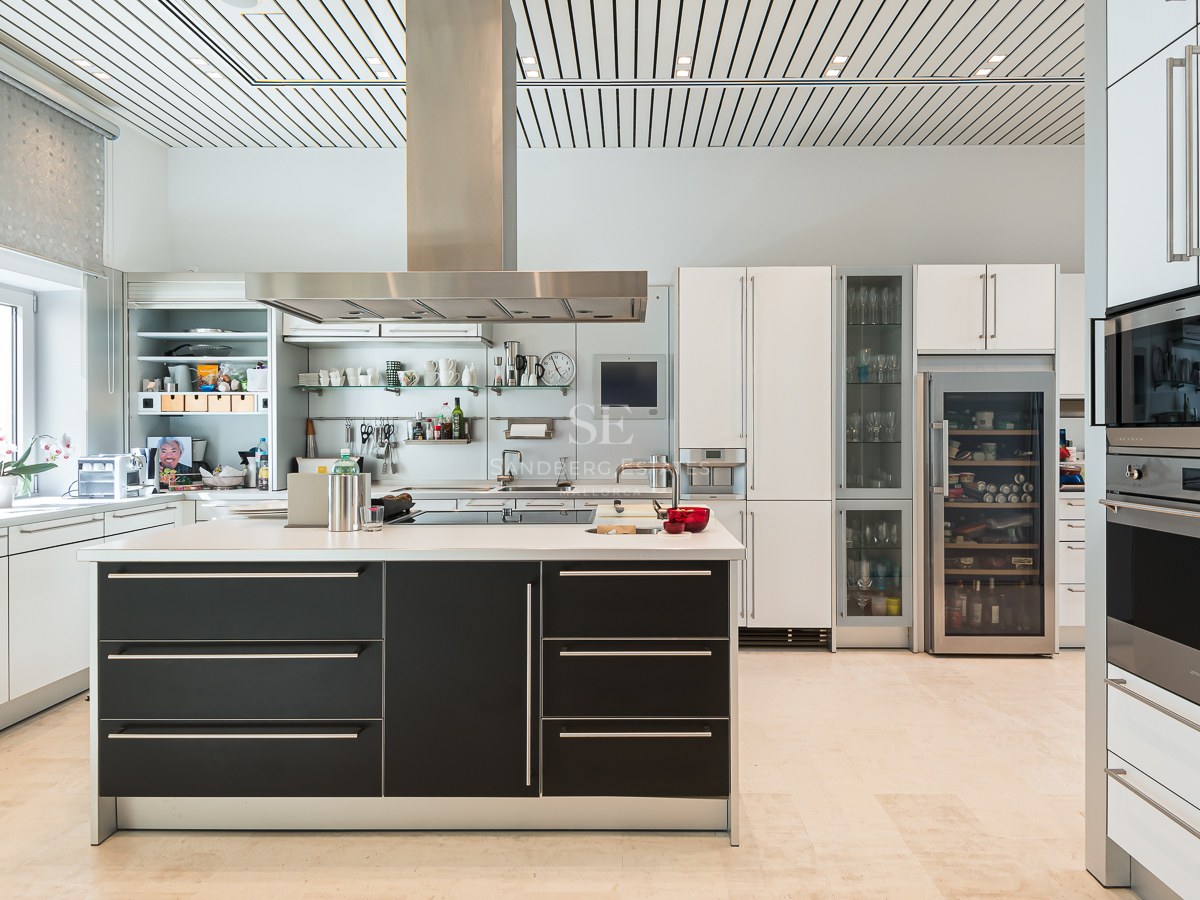 Modern white cabinetry with a black central island, stainless steel appliances, wine fridge, and light stone flooring.