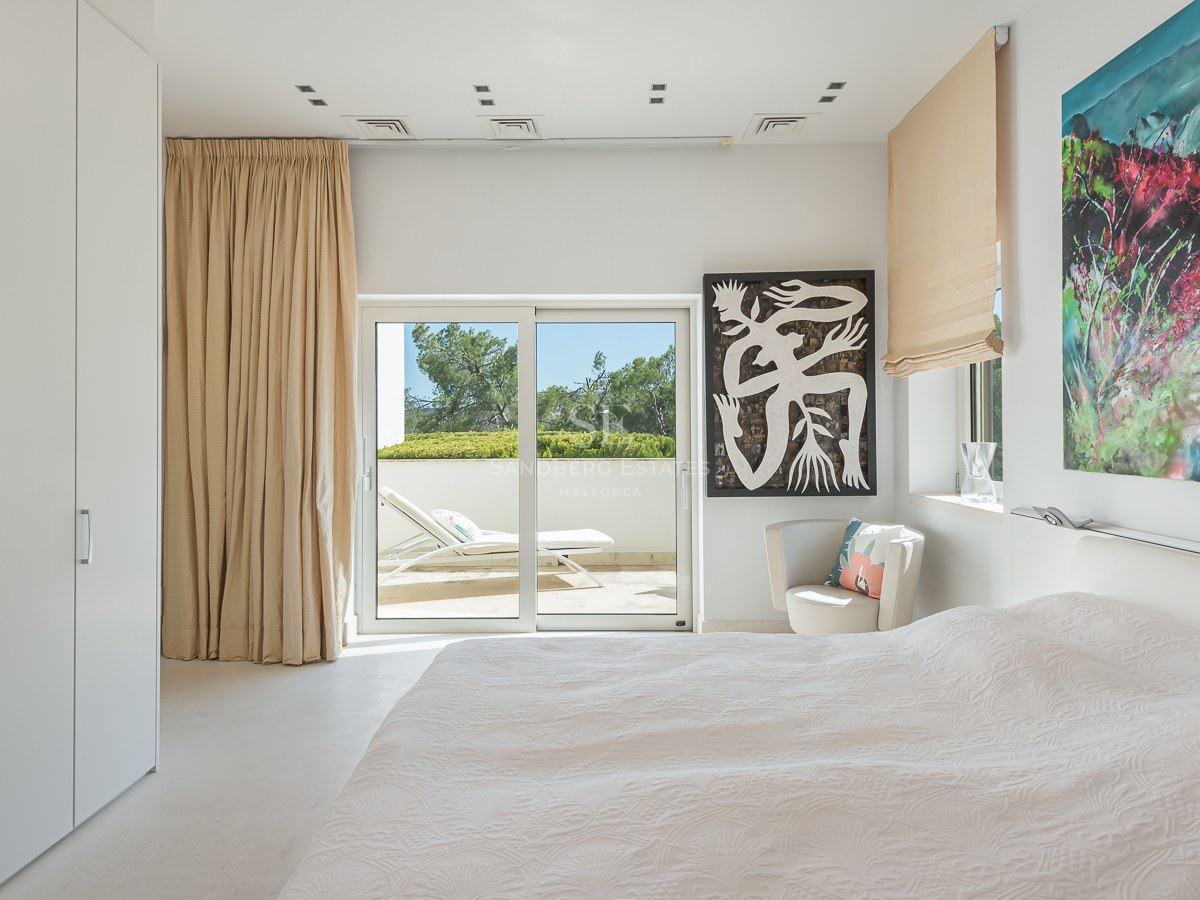 Bright modern bedroom featuring white walls, sliding glass doors to a terrace with sunbed, and colorful contemporary art.
