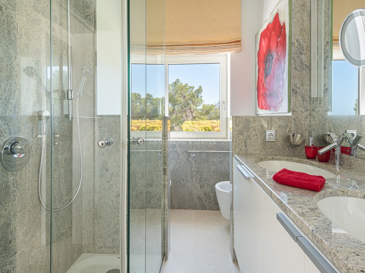 Modern bathroom featuring a granite double vanity, glass walk-in shower, and window with garden views.