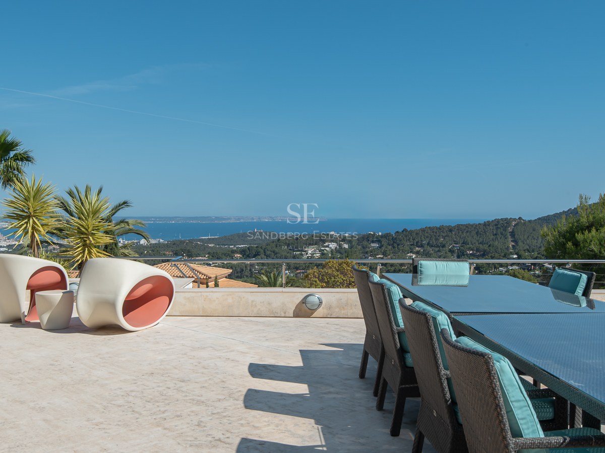 Expansive natural stone terrace with a glass dining table and modern lounge chairs overlooking the bay and mountains.