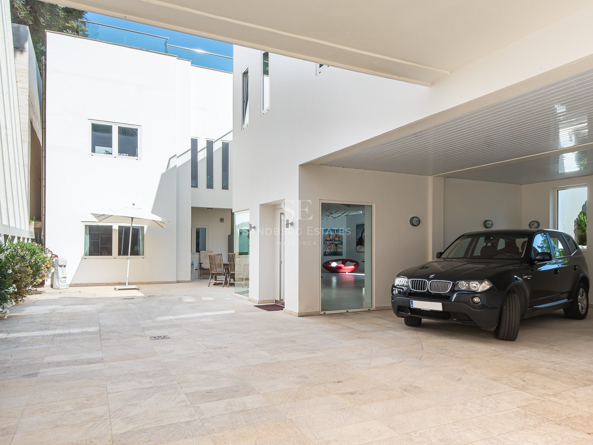 Black SUV parked in a white-walled carport with natural stone paving and bright minimalist architecture.