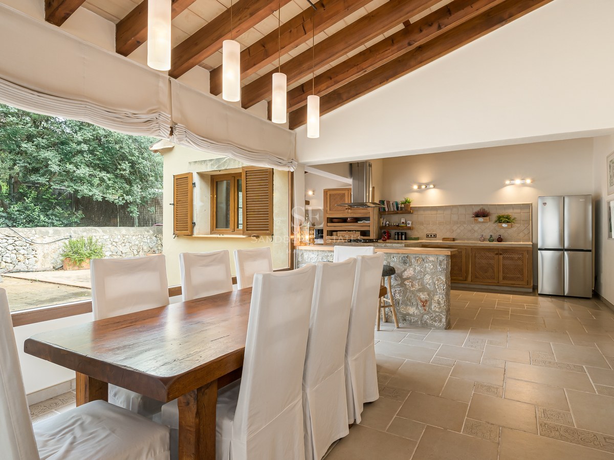 Salle à manger spacieuse avec poutres apparentes, sol en pierre et vue sur le jardin à travers de grandes fenêtres.