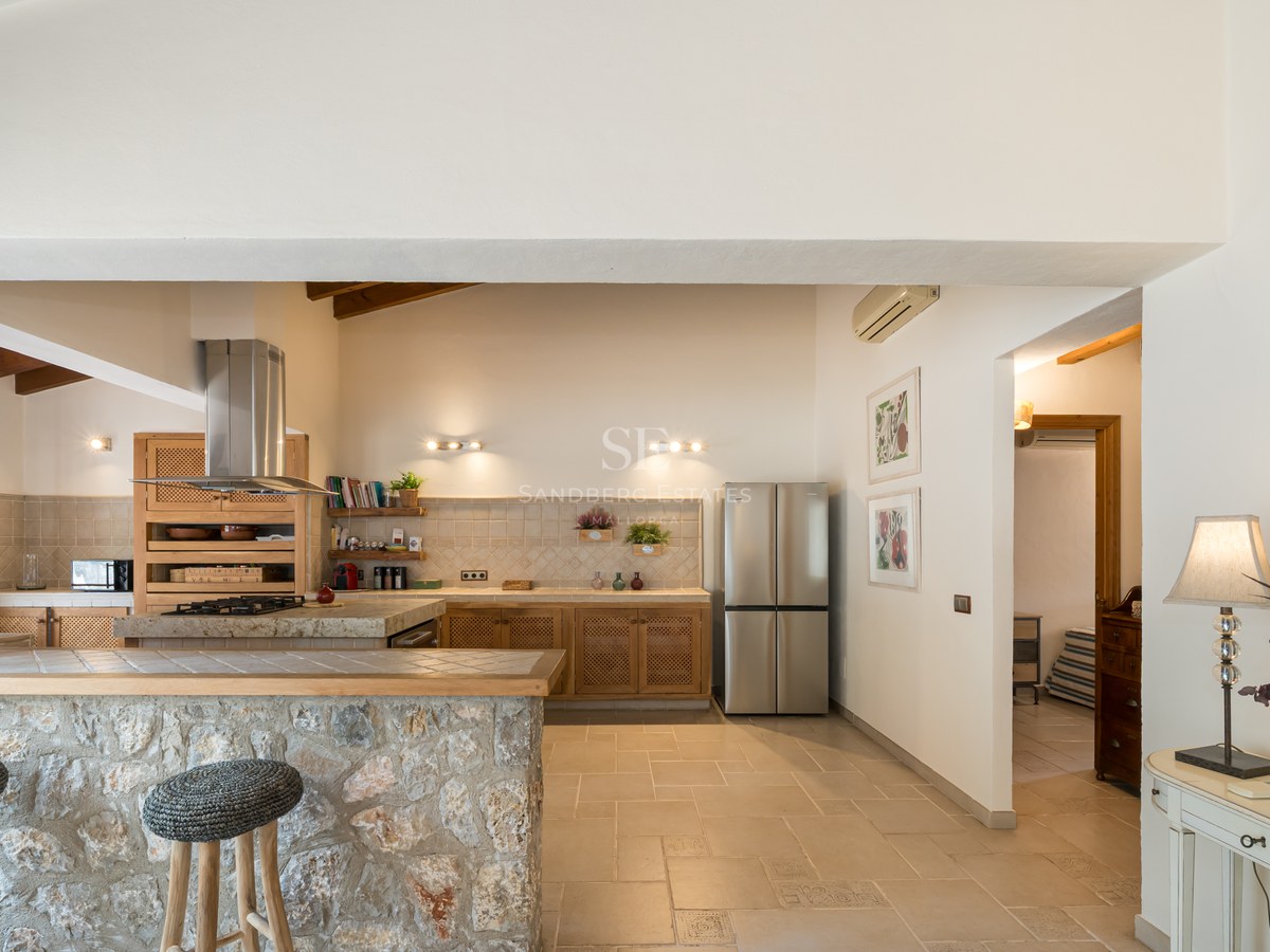 Cuisine spacieuse avec un bar en pierre naturelle, des tabourets, des poutres en bois et des appareils en inox.