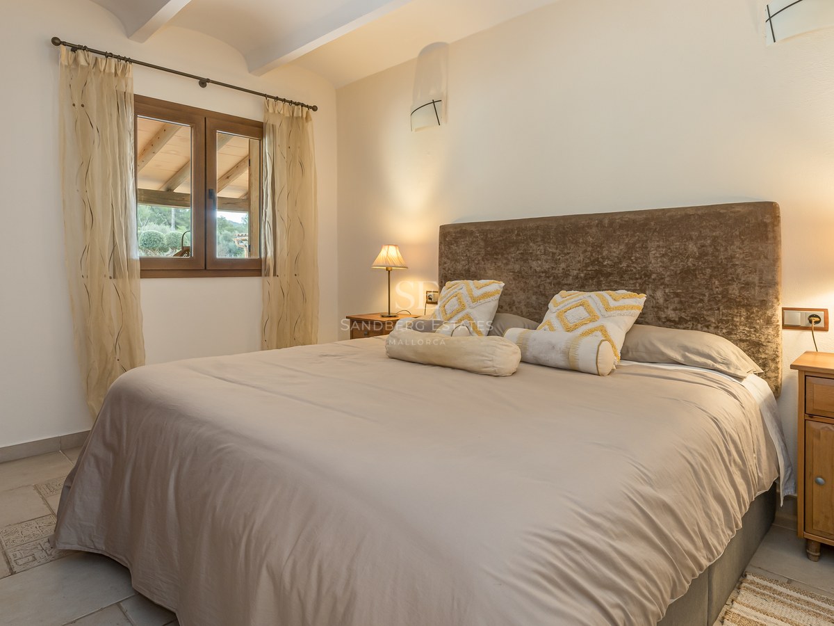 Chambre chaleureuse avec grand lit, tête de lit en velours marron, tables de chevet en bois et éclairage tamisé.