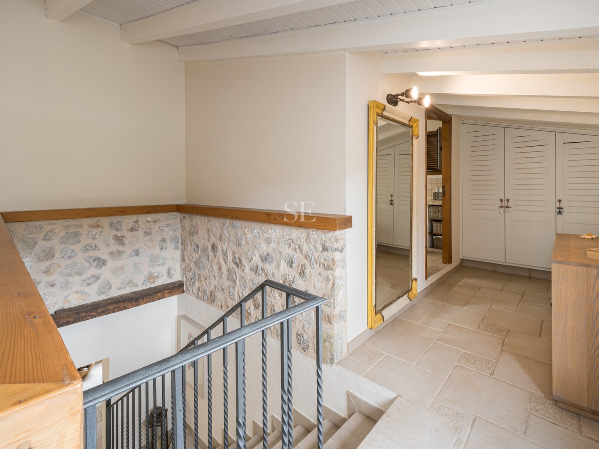 Palier intérieur avec escalier en fer, murs en pierre apparente, poutres en bois et placards intégrés blancs.