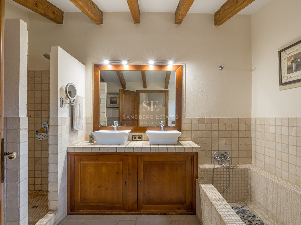 Salle de bain avec double vasque, meuble en bois, poutres apparentes, douche à l'italienne et baignoire carrelée.