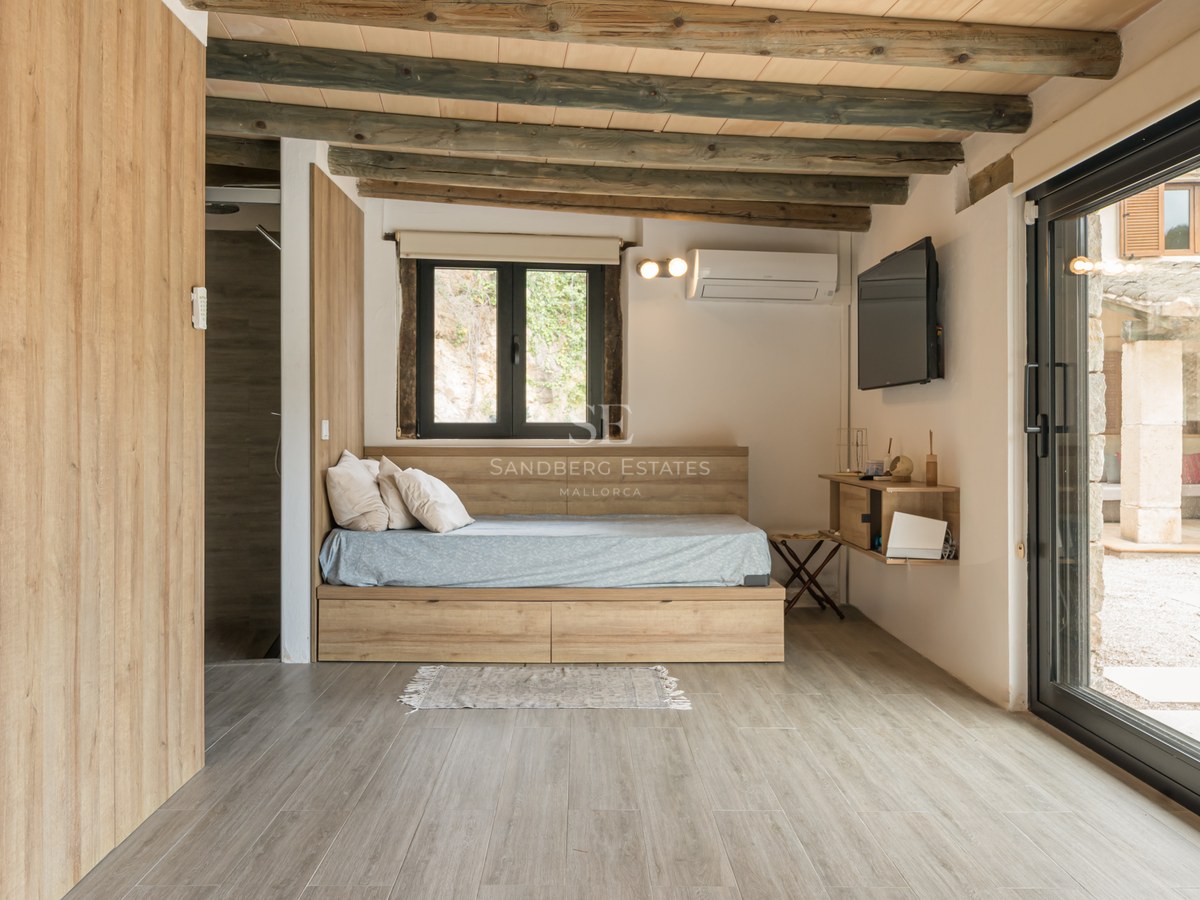 Chambre moderne avec lit plateforme en bois, poutres apparentes et grande porte vitrée donnant sur un patio.