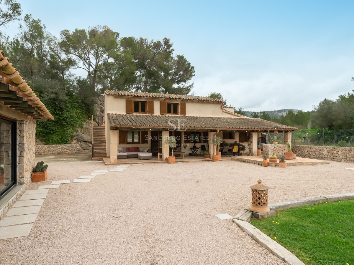 Extérieur d'une maison traditionnelle en pierre avec tuiles en terre cuite, volets en bois et cour en gravier.