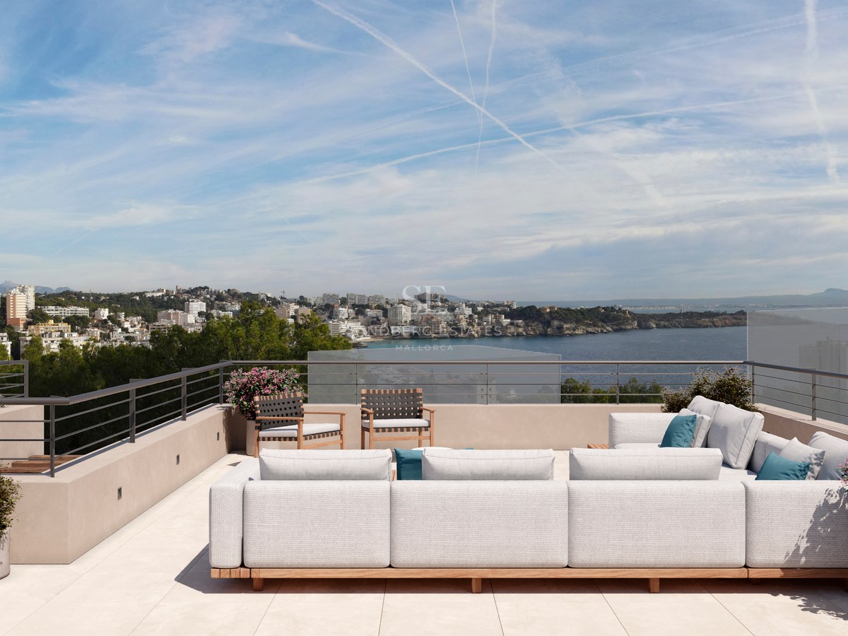 Terrasse de toit moderne avec un grand canapé blanc, des garde-corps en verre et une vue sur une ville côtière.
