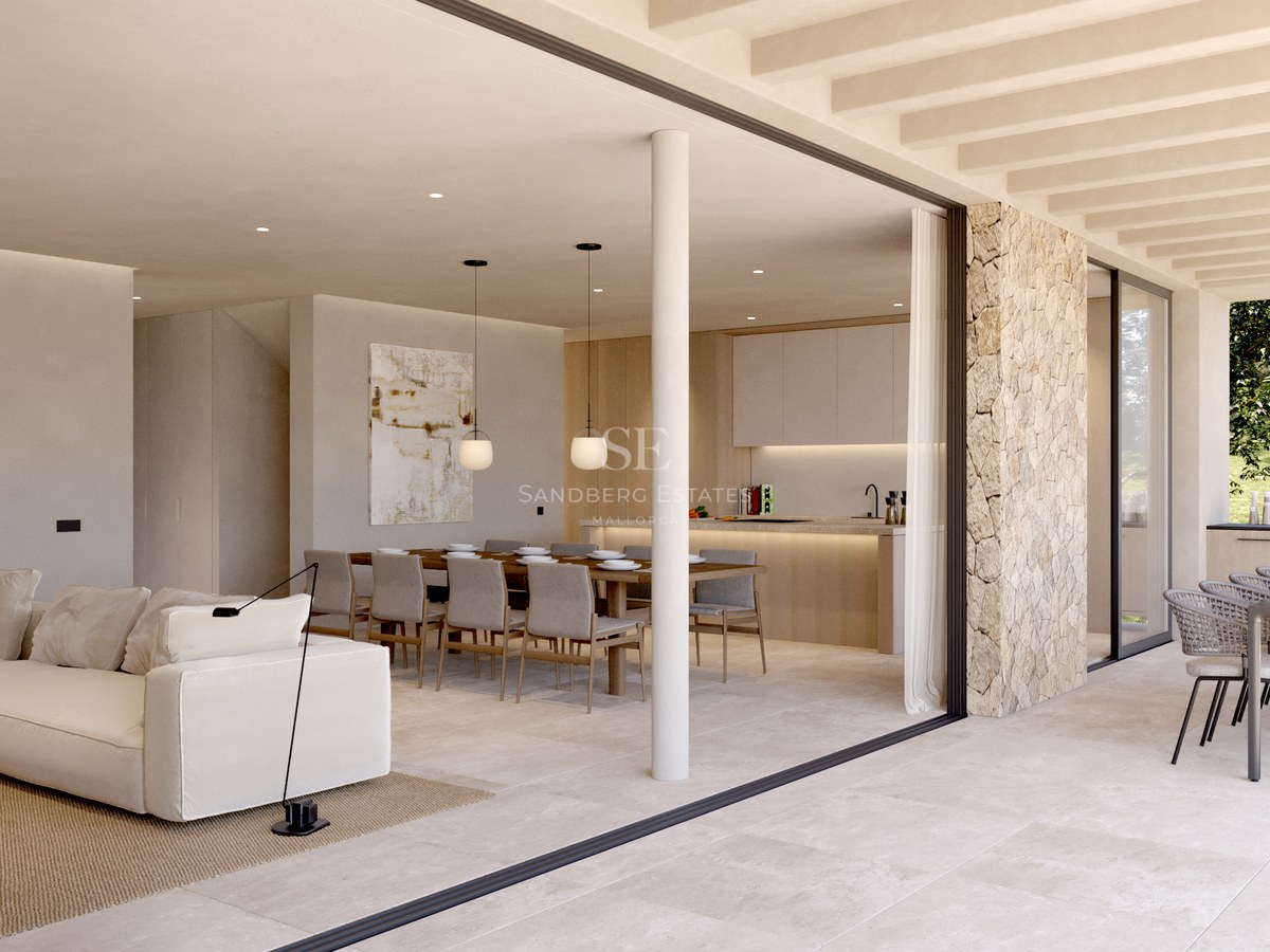 Vaste salon intérieur avec canapé blanc s'ouvrant sur une terrasse extérieure avec coin repas et cuisine.