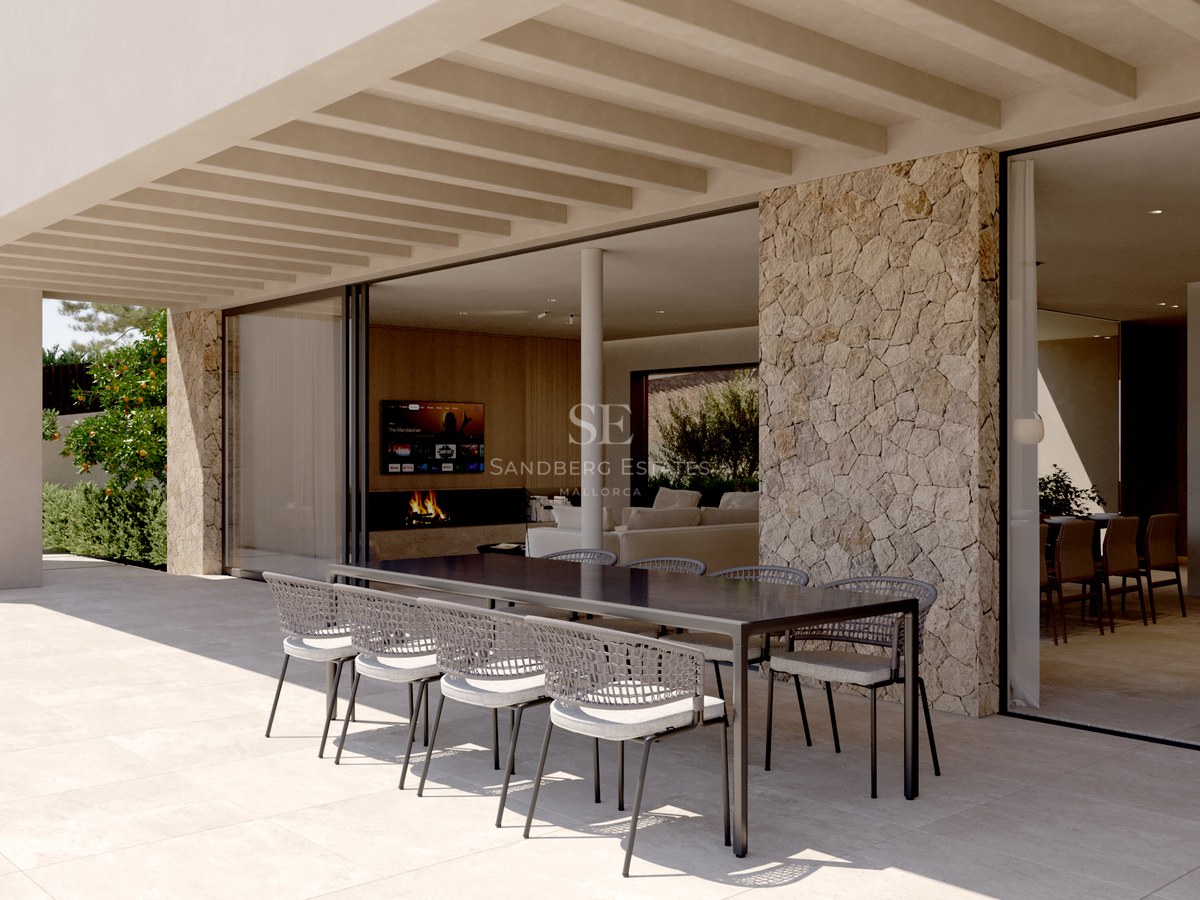 Terrasse moderne couverte avec table noire, chaises tressées, mur en pierre et grandes baies vitrées.