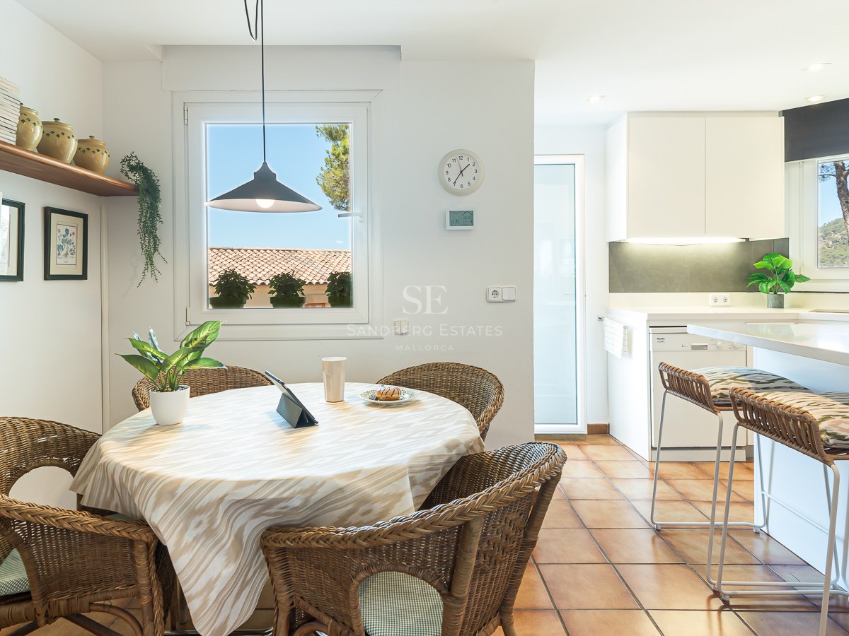 Table à manger ronde avec chaises en osier et sol en terre cuite à côté d'une cuisine moderne blanche.