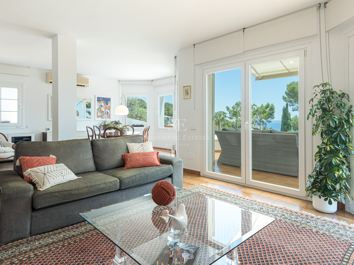 Salon spacieux avec canapé vert, tapis oriental et baies vitrées s'ouvrant sur une terrasse avec vue sur la mer.