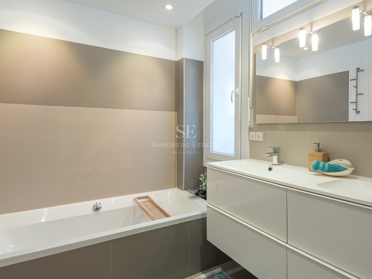 Une salle de bain contemporaine avec baignoire blanche, meuble double vasque, grands carreaux beiges et un large miroir.