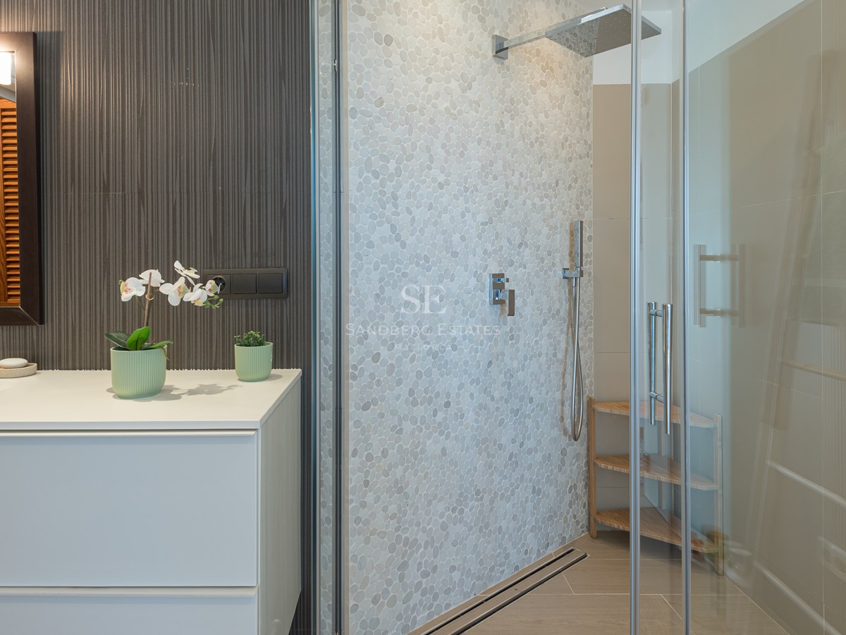 Salle de bain contemporaine avec meuble vasque blanc et douche en verre avec mur en galets texturés.