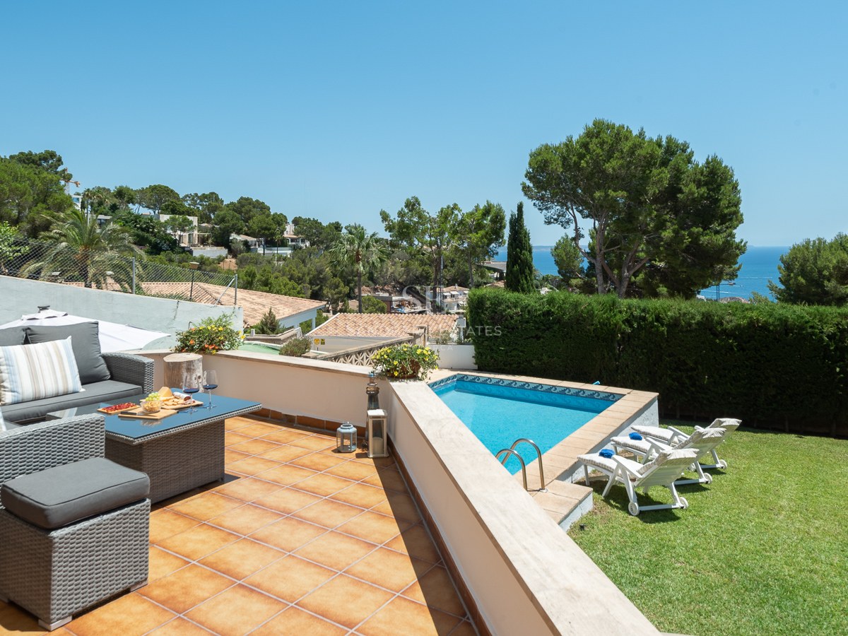Terrasse ensoleillée avec canapés en résine tressée, piscine bleue, pelouse et vue panoramique sur l'océan.