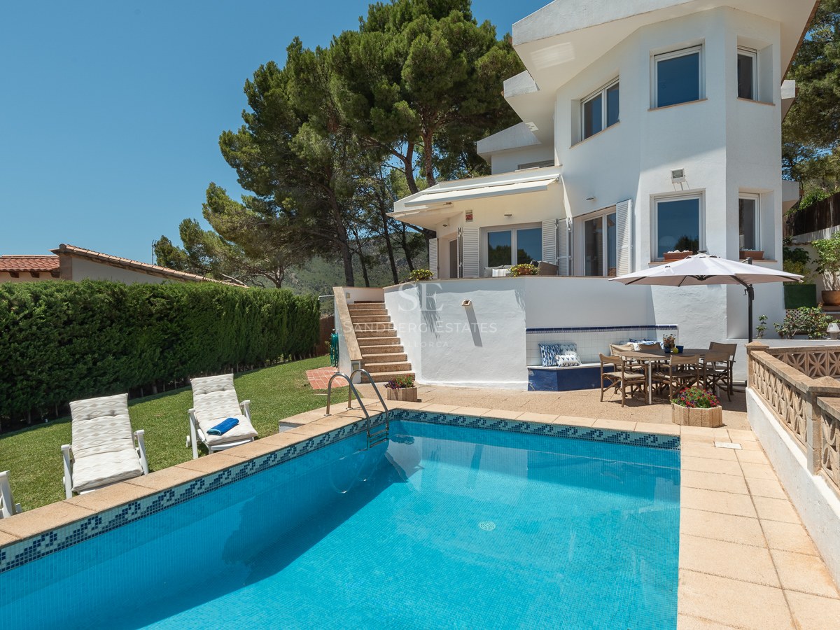Villa blanche avec piscine carrelée bleue, pelouse avec transats et espace repas extérieur avec parasol.