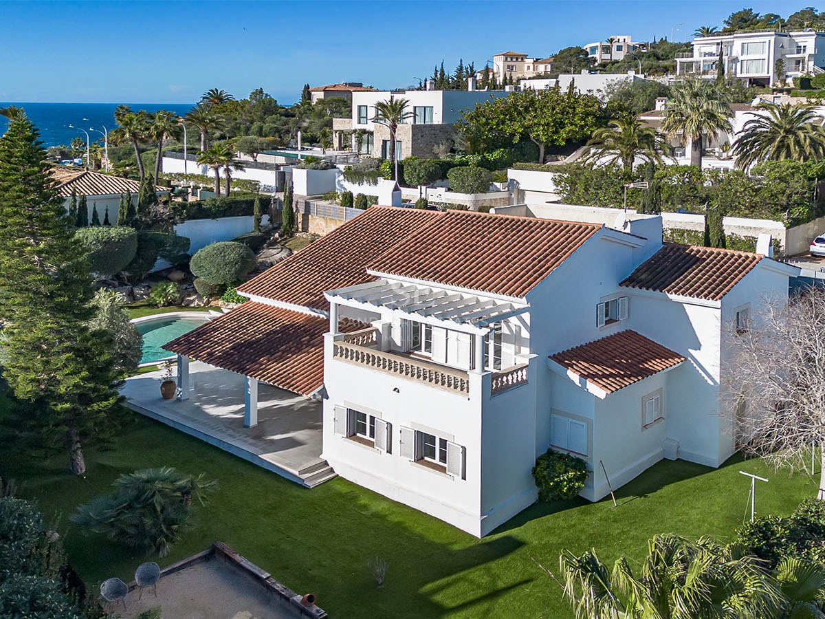 Vue aérienne d'une villa blanche méditerranéenne, toit en terre cuite, jardin, piscine et mer en arrière-plan.