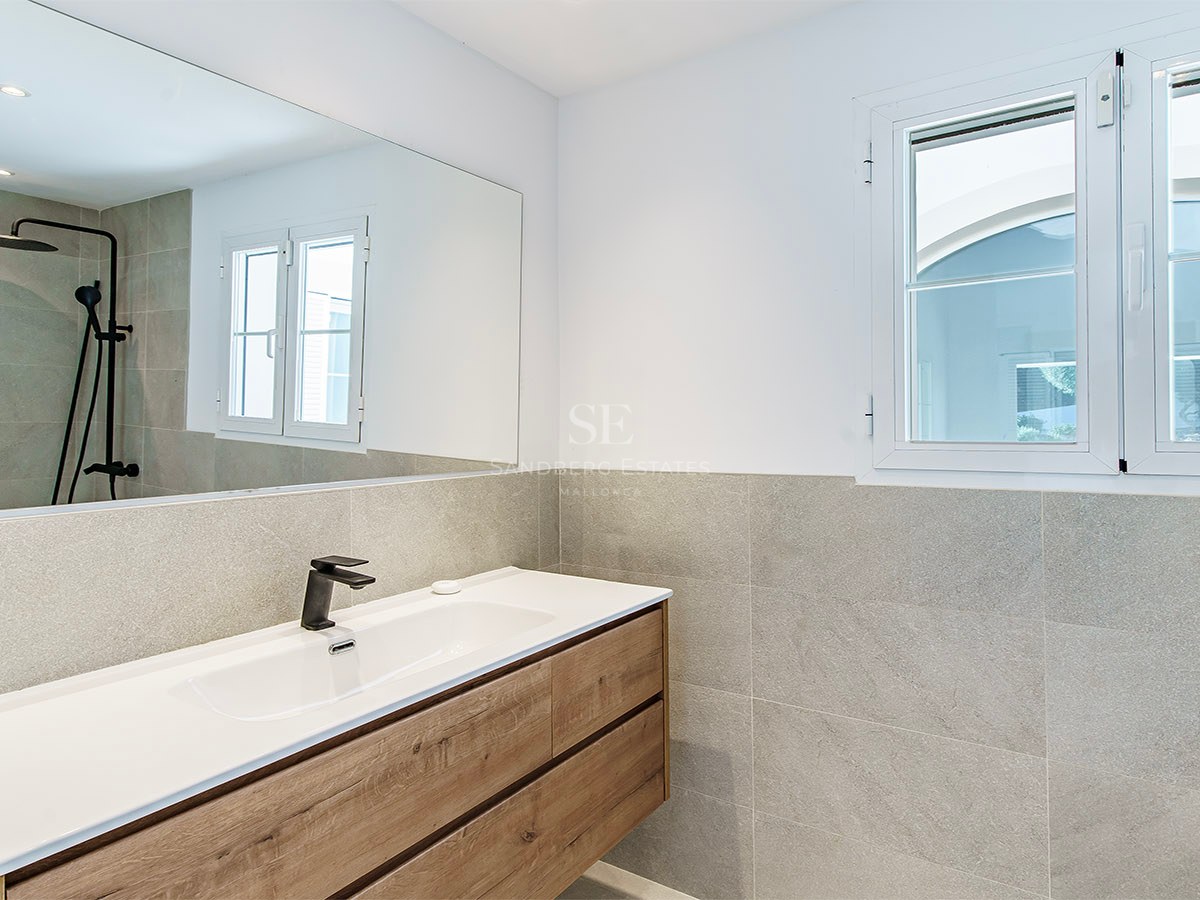 Intérieur d'une salle de bain moderne avec meuble en bois, lavabo blanc, robinetterie noire et carrelage gris.