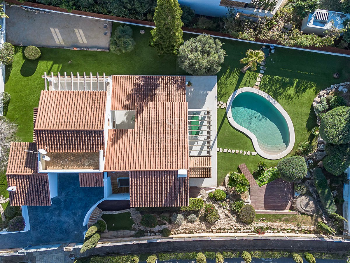 Vue plongeante d'une villa de luxe avec toit en terre cuite, piscine en forme de rein et jardins paysagers.