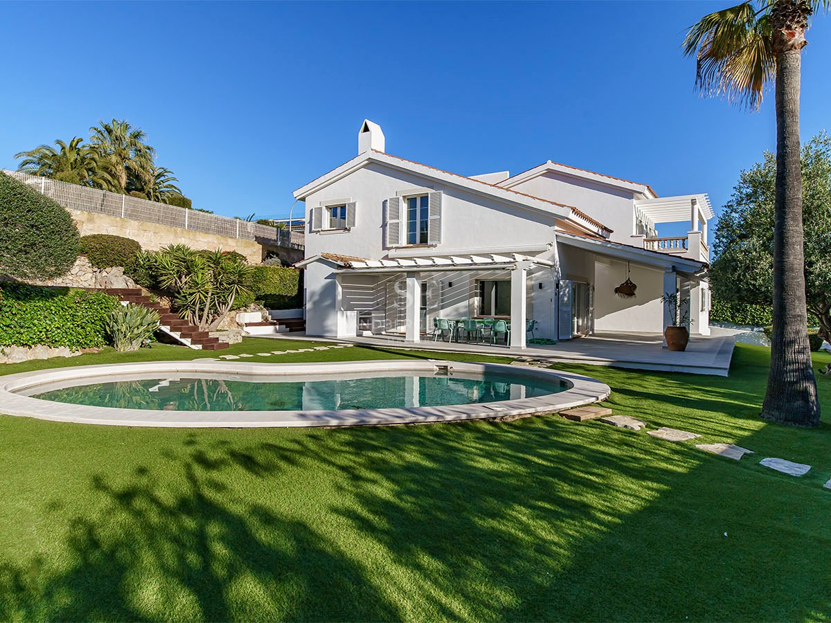 Villa blanche à deux étages avec piscine de forme organique, pelouse verte et palmiers sous un ciel bleu clair.