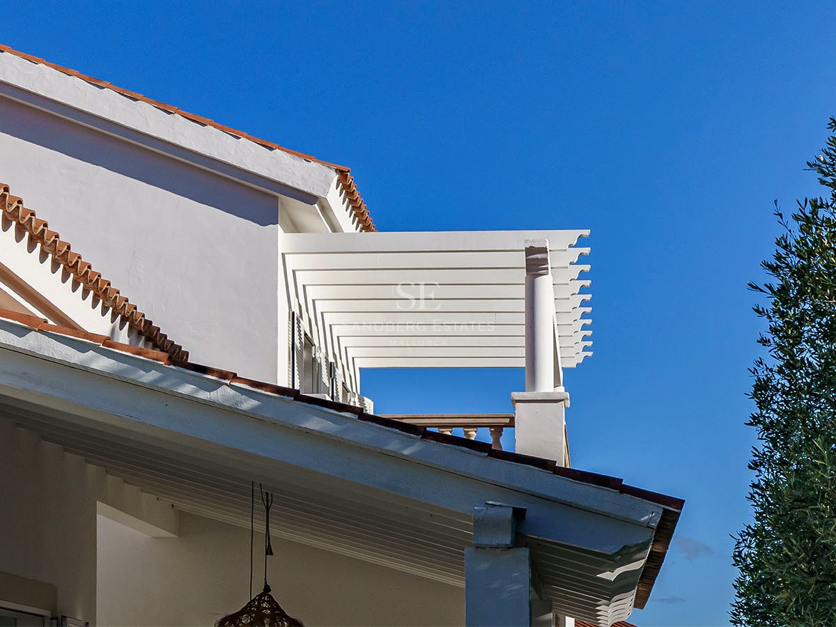 Détail de façade d'une villa blanche avec pergola, tuiles en terre cuite et ciel bleu azur.