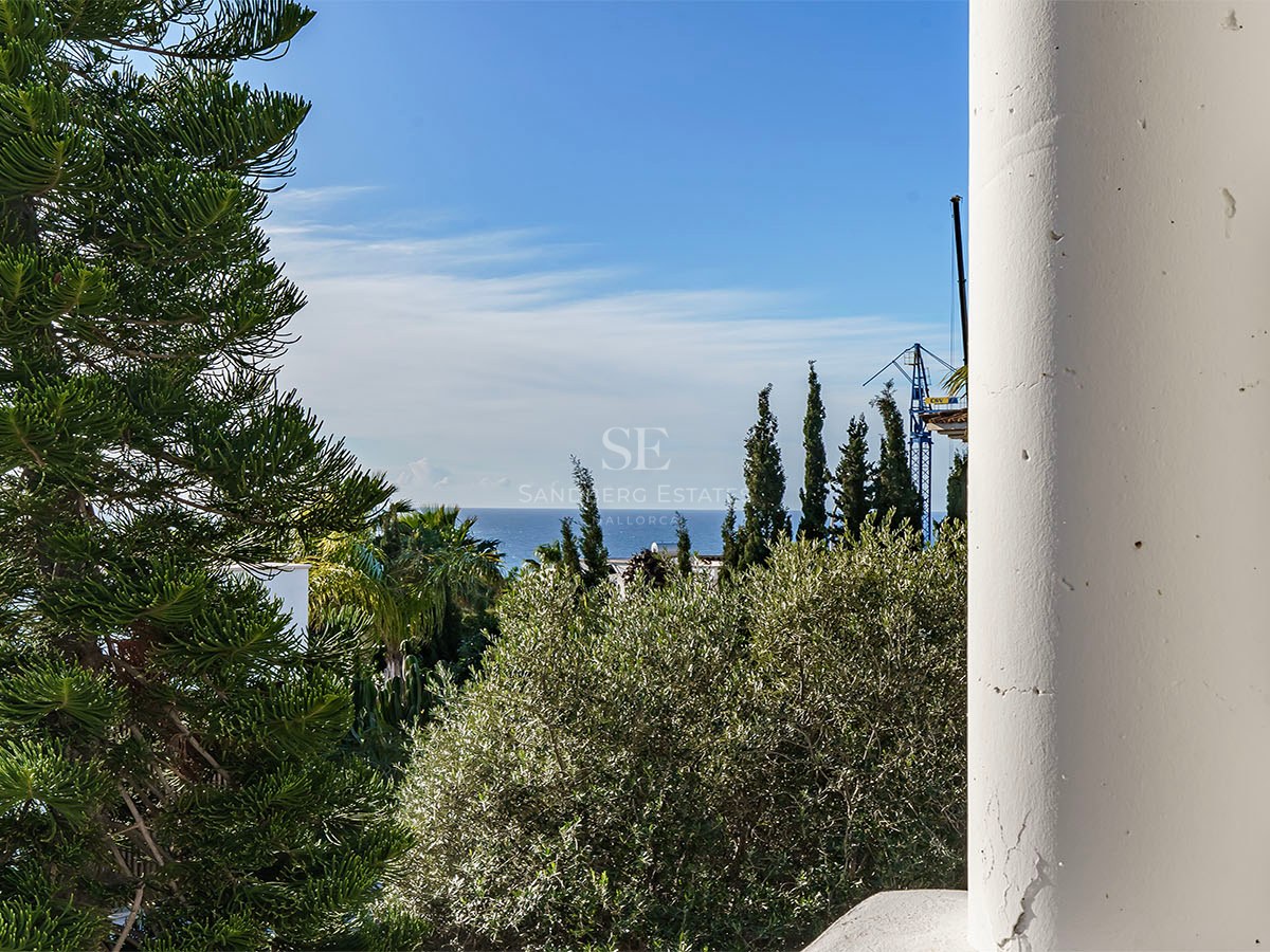Vue sur la mer Méditerranée encadrée par une colonne blanche et une végétation luxuriante sous un ciel bleu.