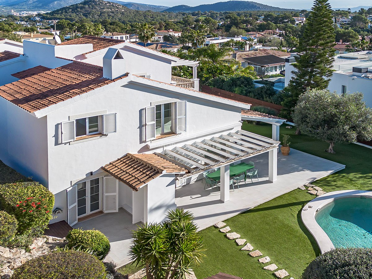 Vue aérienne d'une villa blanche avec toit en tuiles, jardin verdoyant, pergola et piscine privée.